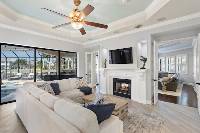 living room featuring crown molding, a tray ceiling, ceiling fan, and light wood-type flooring