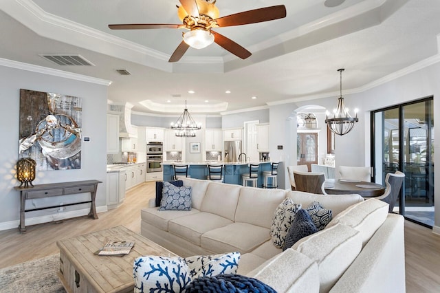 living room with a raised ceiling, crown molding, ceiling fan with notable chandelier, and light wood-type flooring