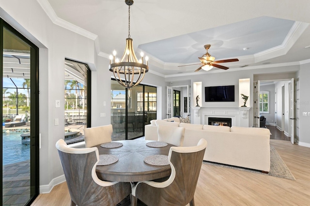 dining area with ornamental molding, ceiling fan with notable chandelier, light hardwood / wood-style floors, and a tray ceiling