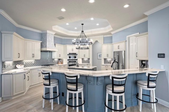 kitchen with a breakfast bar area, light hardwood / wood-style floors, a tray ceiling, stainless steel appliances, and wall chimney range hood