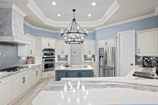 kitchen with sink, hanging light fixtures, a kitchen island with sink, a tray ceiling, and stainless steel appliances