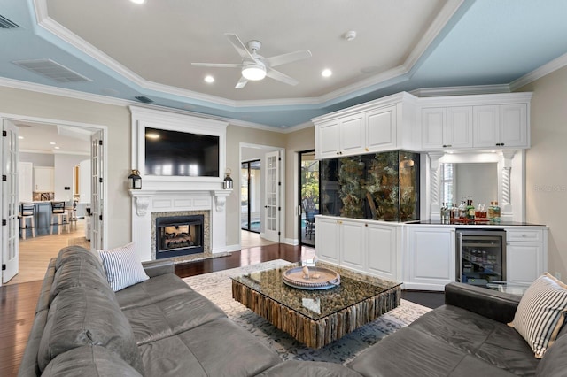 living room featuring crown molding, hardwood / wood-style flooring, a raised ceiling, beverage cooler, and indoor bar