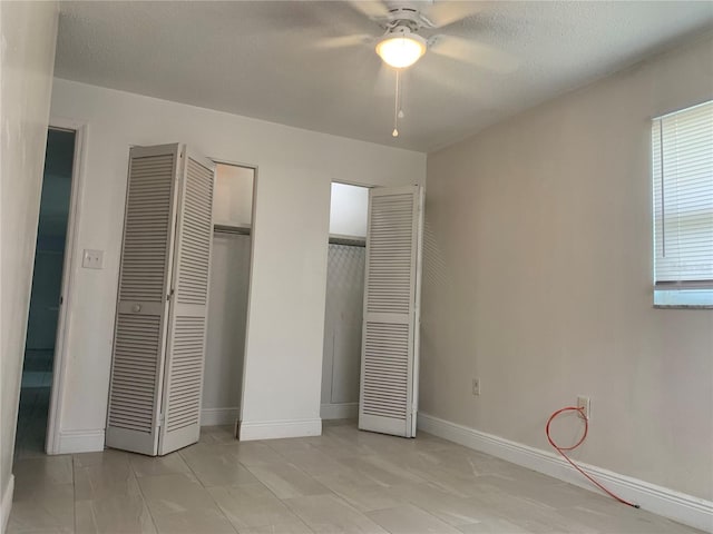 unfurnished bedroom featuring ceiling fan, a textured ceiling, and multiple closets