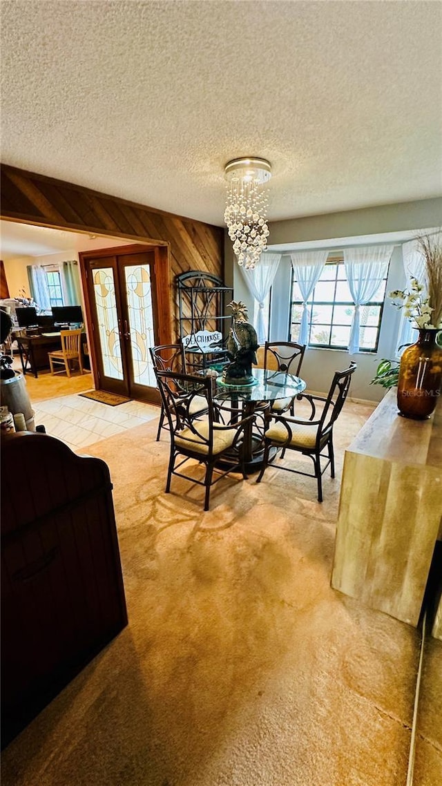 carpeted dining space featuring wood walls, a notable chandelier, a textured ceiling, and french doors