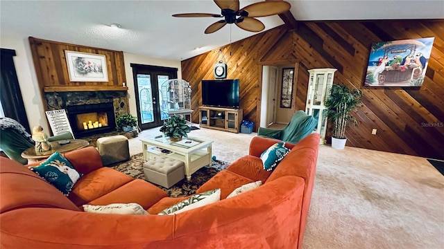 carpeted living room with lofted ceiling, ceiling fan, a stone fireplace, french doors, and wood walls