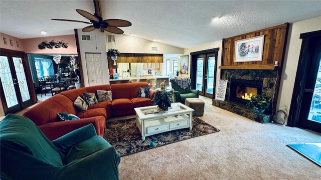 living room with vaulted ceiling, a stone fireplace, carpet flooring, a textured ceiling, and french doors