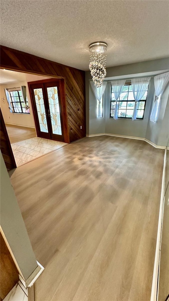 1670 Monterey Dr, Clearwater, FL 33756 - unfurnished dining area with healthy amount of natural light, a chandelier, a textured ceiling, french doors, and wooden walls