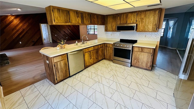 1670 Monterey Dr, Clearwater, FL 33756 - kitchen featuring stainless steel appliances, a sink, light countertops, brown cabinetry, and wood walls