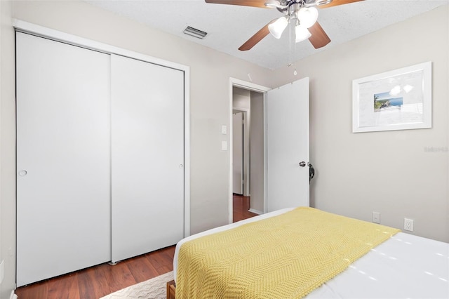 bedroom with a textured ceiling, dark wood-type flooring, a closet, and ceiling fan