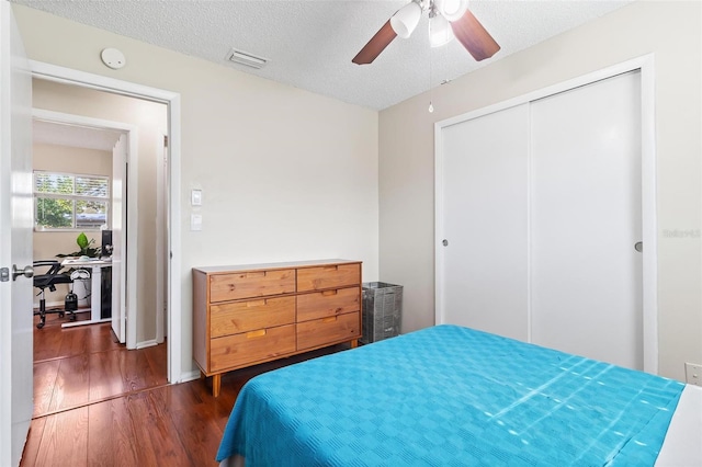 bedroom with ceiling fan, dark hardwood / wood-style floors, a textured ceiling, and a closet