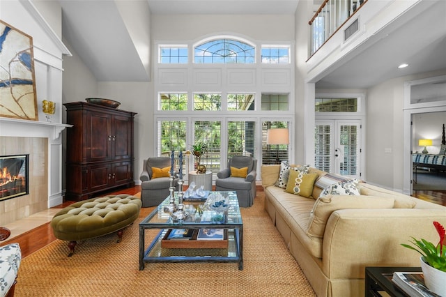 living room with a high ceiling, a tile fireplace, light wood-type flooring, and french doors