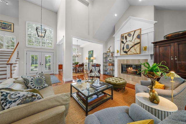 living room featuring a tile fireplace, hardwood / wood-style floors, high vaulted ceiling, french doors, and a chandelier