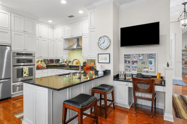 kitchen with sink, a breakfast bar area, kitchen peninsula, stainless steel appliances, and wall chimney range hood