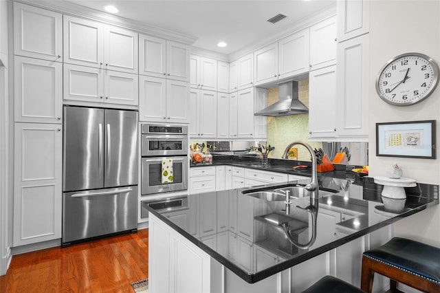 kitchen with wall chimney exhaust hood, white cabinetry, appliances with stainless steel finishes, and kitchen peninsula