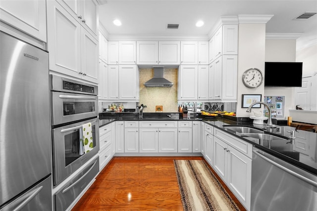 kitchen featuring wall chimney range hood, sink, dark wood-type flooring, appliances with stainless steel finishes, and white cabinets