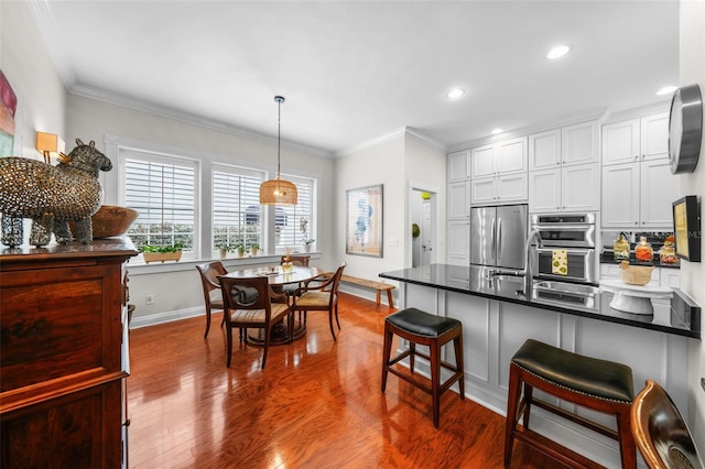 kitchen with pendant lighting, crown molding, white cabinetry, stainless steel appliances, and a kitchen bar