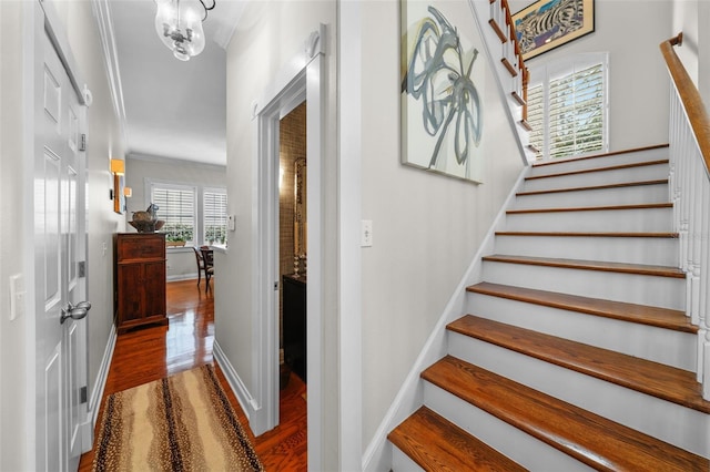 staircase with hardwood / wood-style flooring, crown molding, and an inviting chandelier