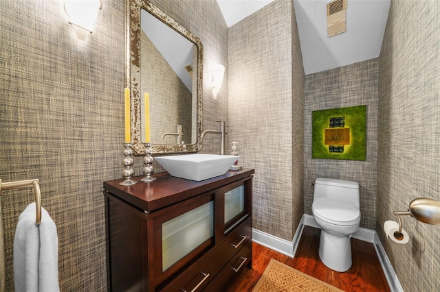 bathroom featuring hardwood / wood-style flooring, vaulted ceiling, vanity, and toilet