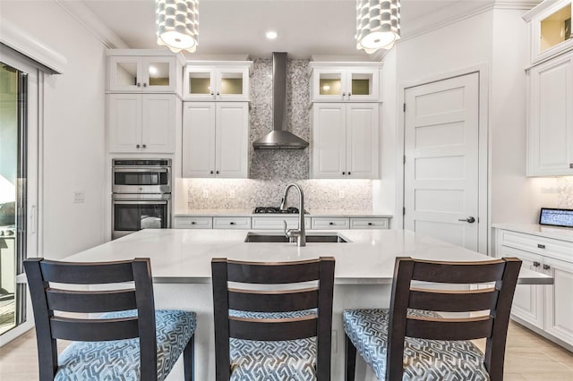 kitchen with white cabinets, double oven, hanging light fixtures, and wall chimney range hood