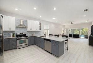 kitchen with white cabinetry, appliances with stainless steel finishes, gray cabinetry, and wall chimney exhaust hood