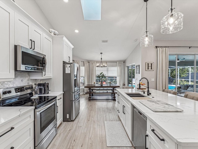 kitchen with hanging light fixtures, white cabinetry, appliances with stainless steel finishes, and a sink