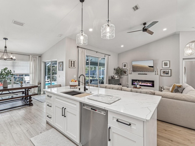 kitchen with white cabinets, open floor plan, hanging light fixtures, stainless steel dishwasher, and a sink