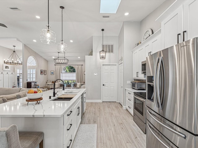 kitchen with white cabinets, an island with sink, appliances with stainless steel finishes, open floor plan, and pendant lighting