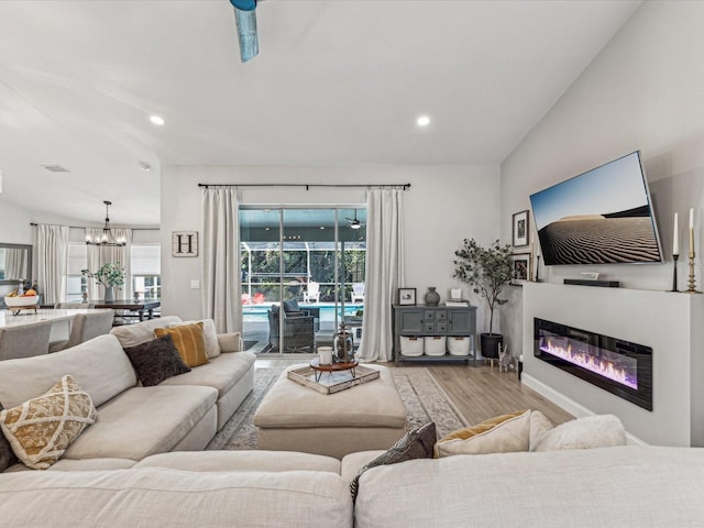 living area with a notable chandelier, wood finished floors, a glass covered fireplace, and recessed lighting