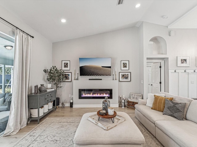 living area with lofted ceiling, recessed lighting, baseboards, light wood finished floors, and a glass covered fireplace