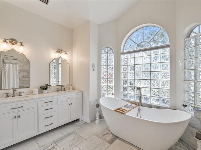 full bath with marble finish floor, double vanity, a soaking tub, and a sink