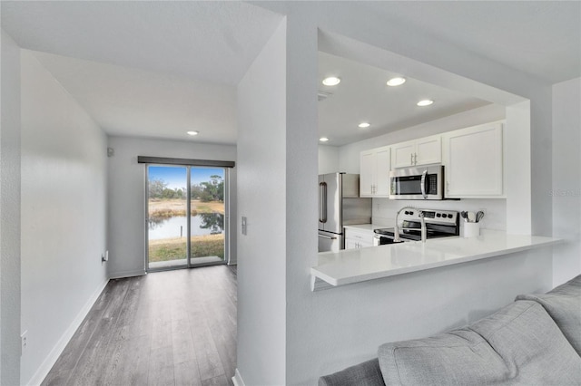 kitchen featuring a water view, light wood-type flooring, kitchen peninsula, stainless steel appliances, and white cabinets