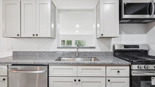 kitchen featuring appliances with stainless steel finishes, sink, white cabinets, and light stone counters