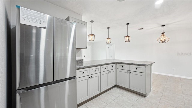 kitchen with stone countertops, hanging light fixtures, light tile patterned floors, stainless steel fridge, and kitchen peninsula