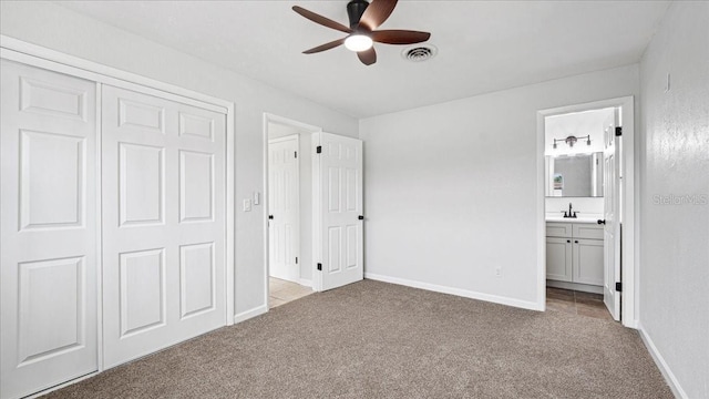 unfurnished bedroom featuring ensuite bathroom, sink, light colored carpet, a closet, and ceiling fan