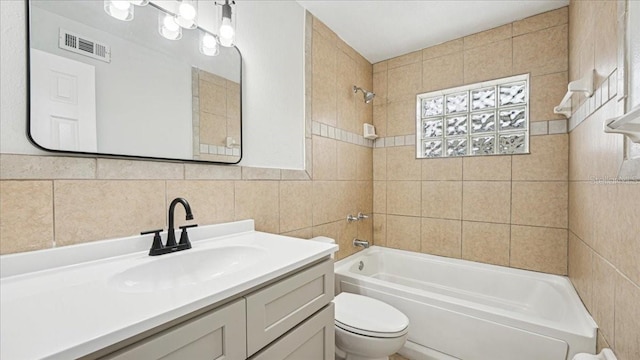 full bathroom with tiled shower / bath, vanity, toilet, and tile walls