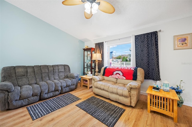 living room featuring lofted ceiling, ceiling fan, wood-type flooring, and a textured ceiling