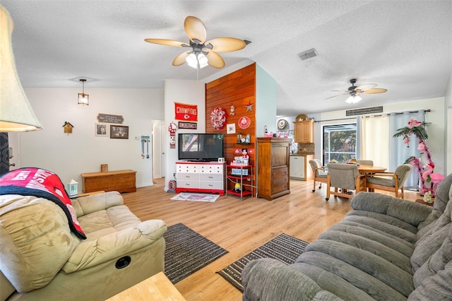 living room featuring light hardwood / wood-style flooring, a textured ceiling, vaulted ceiling, and ceiling fan