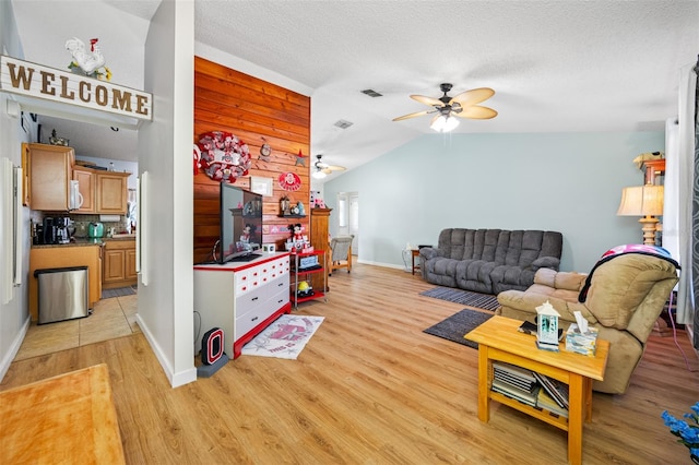 living room with ceiling fan, lofted ceiling, a textured ceiling, and light hardwood / wood-style floors