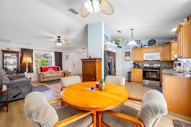 dining space with ceiling fan, sink, vaulted ceiling, and light hardwood / wood-style flooring