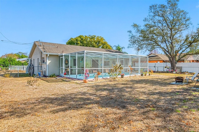 back of property with a pool, a yard, glass enclosure, and a fire pit