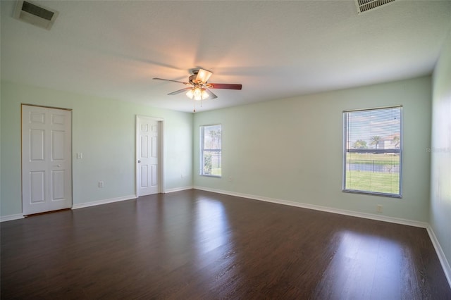 empty room featuring ceiling fan, dark wood-type flooring, visible vents, and baseboards