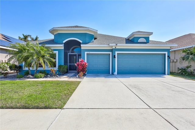 view of front facade with stucco siding, driveway, a front lawn, and a garage