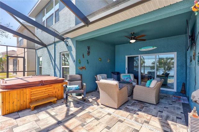 view of patio with glass enclosure, a hot tub, and a ceiling fan