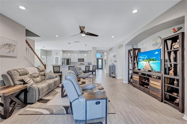 living room with light wood-style flooring, recessed lighting, arched walkways, ceiling fan, and stairs