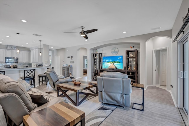 living area with a ceiling fan, recessed lighting, visible vents, and arched walkways