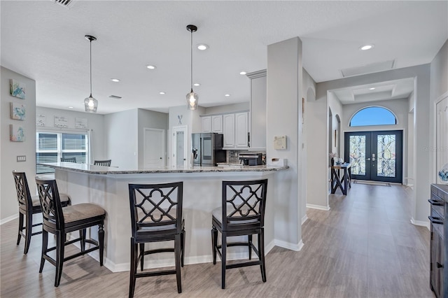 kitchen with a breakfast bar area, stainless steel fridge with ice dispenser, french doors, and a healthy amount of sunlight