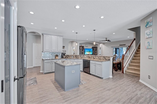 kitchen with arched walkways, a peninsula, a kitchen island, and black dishwasher