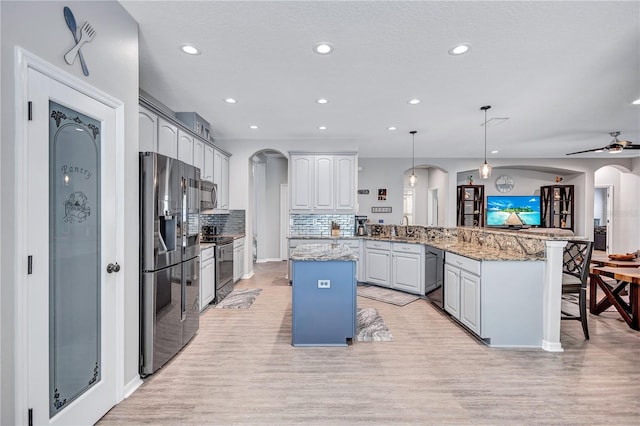 kitchen with black appliances, a kitchen breakfast bar, arched walkways, a peninsula, and light wood finished floors