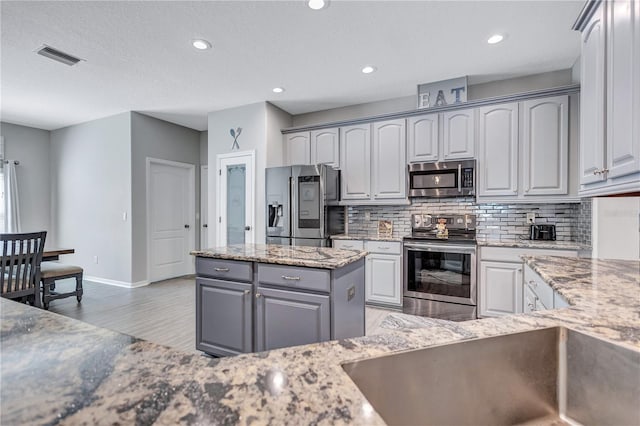 kitchen featuring decorative backsplash, stainless steel appliances, visible vents, and light stone countertops