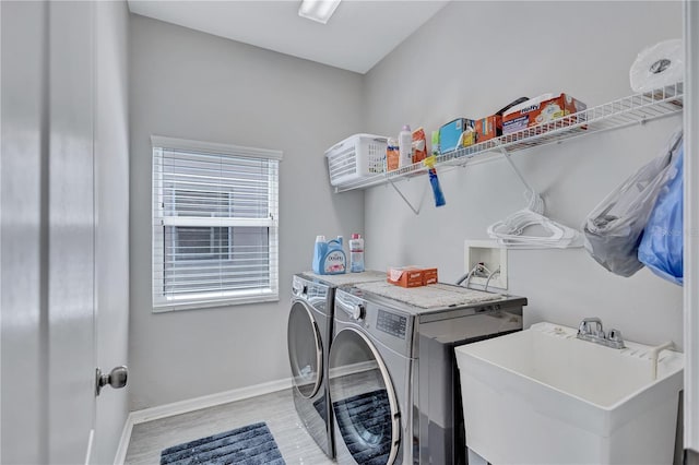 washroom with baseboards, light wood finished floors, laundry area, separate washer and dryer, and a sink